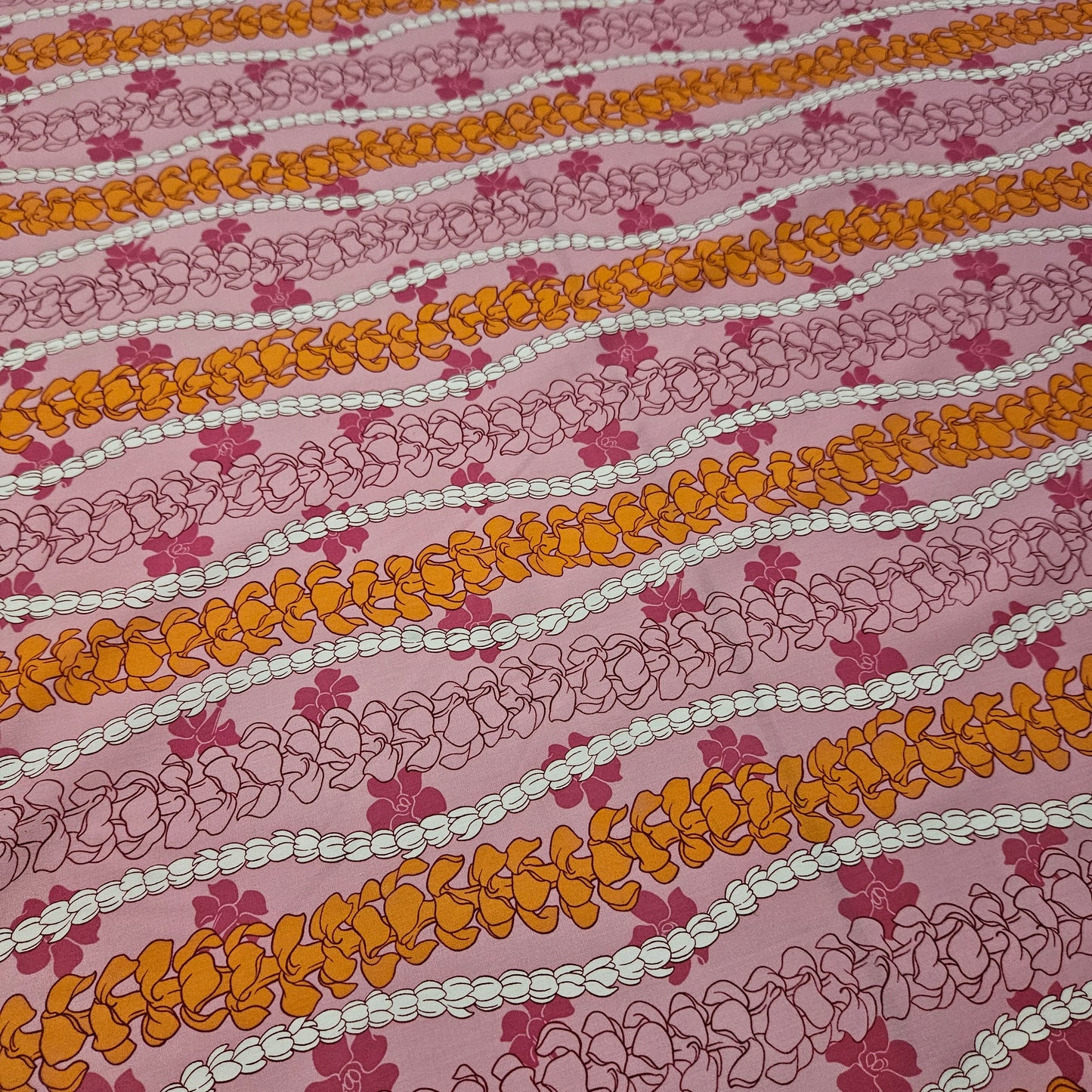 Patterned fabric with orange, white, and pink floral design on a pink background