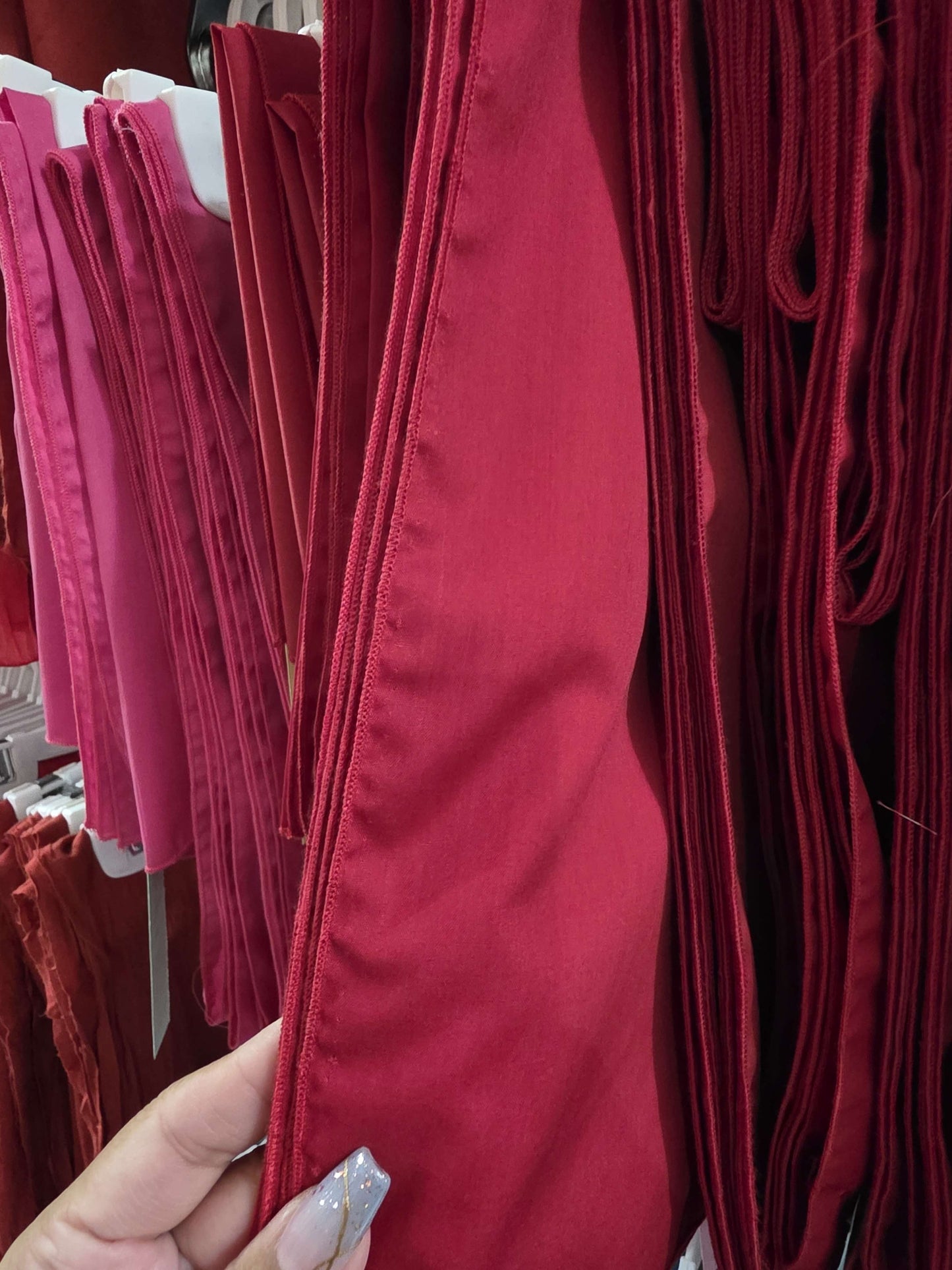 Close-up of red fabric without fringe held by a hand, with more fabric in the background.