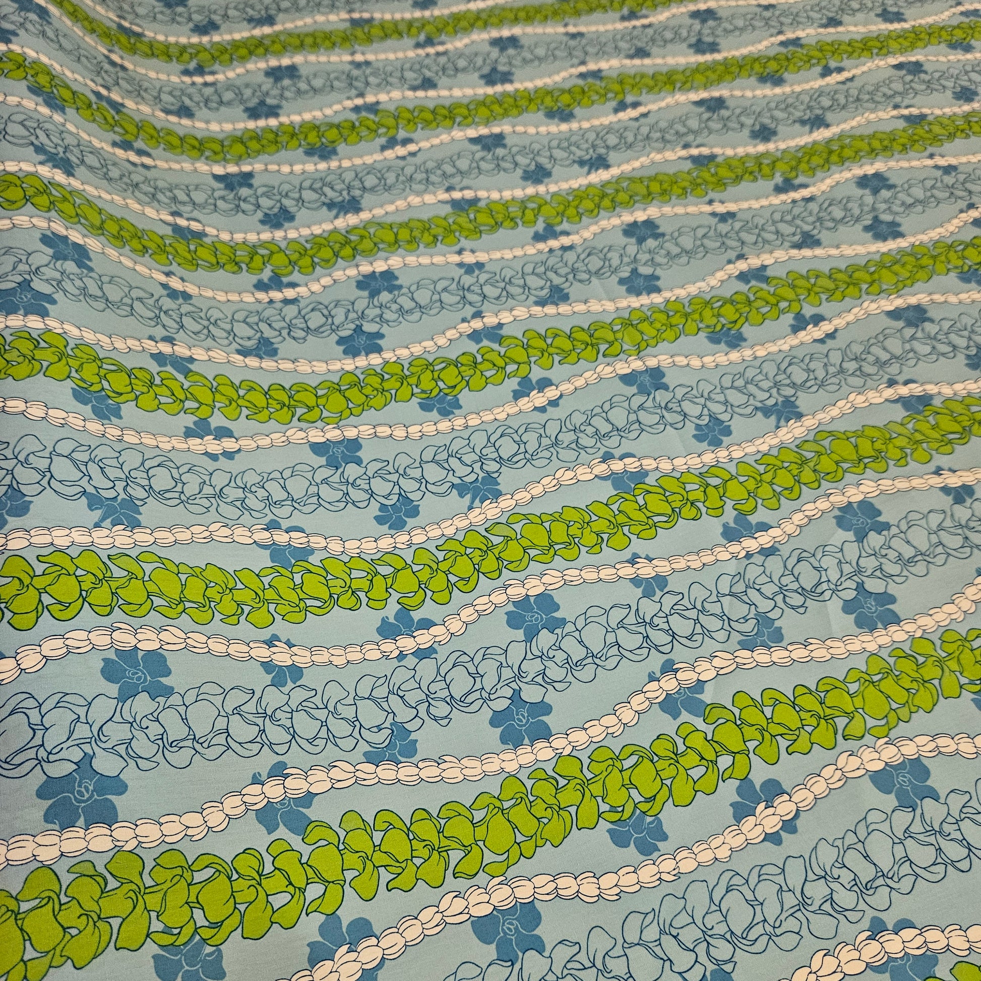 Patterned fabric with green, blue, and beige wavy floral lines on a light blue background