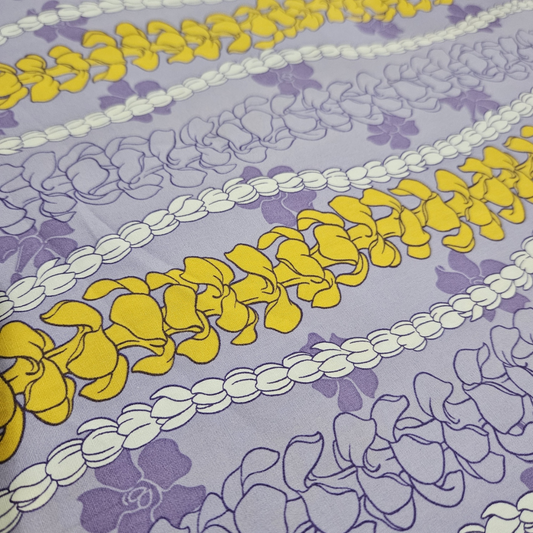 Patterned fabric with yellow floral shapes and white and purple floral designs on a light purple background.
